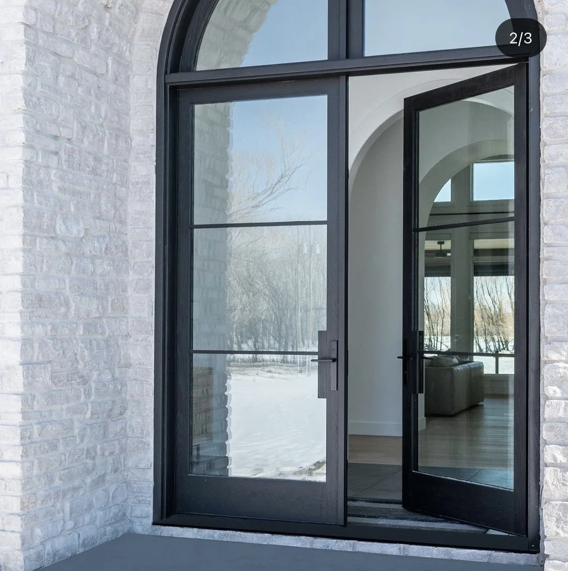 Arched black steel double entry doors with glass in a white brick Austin home