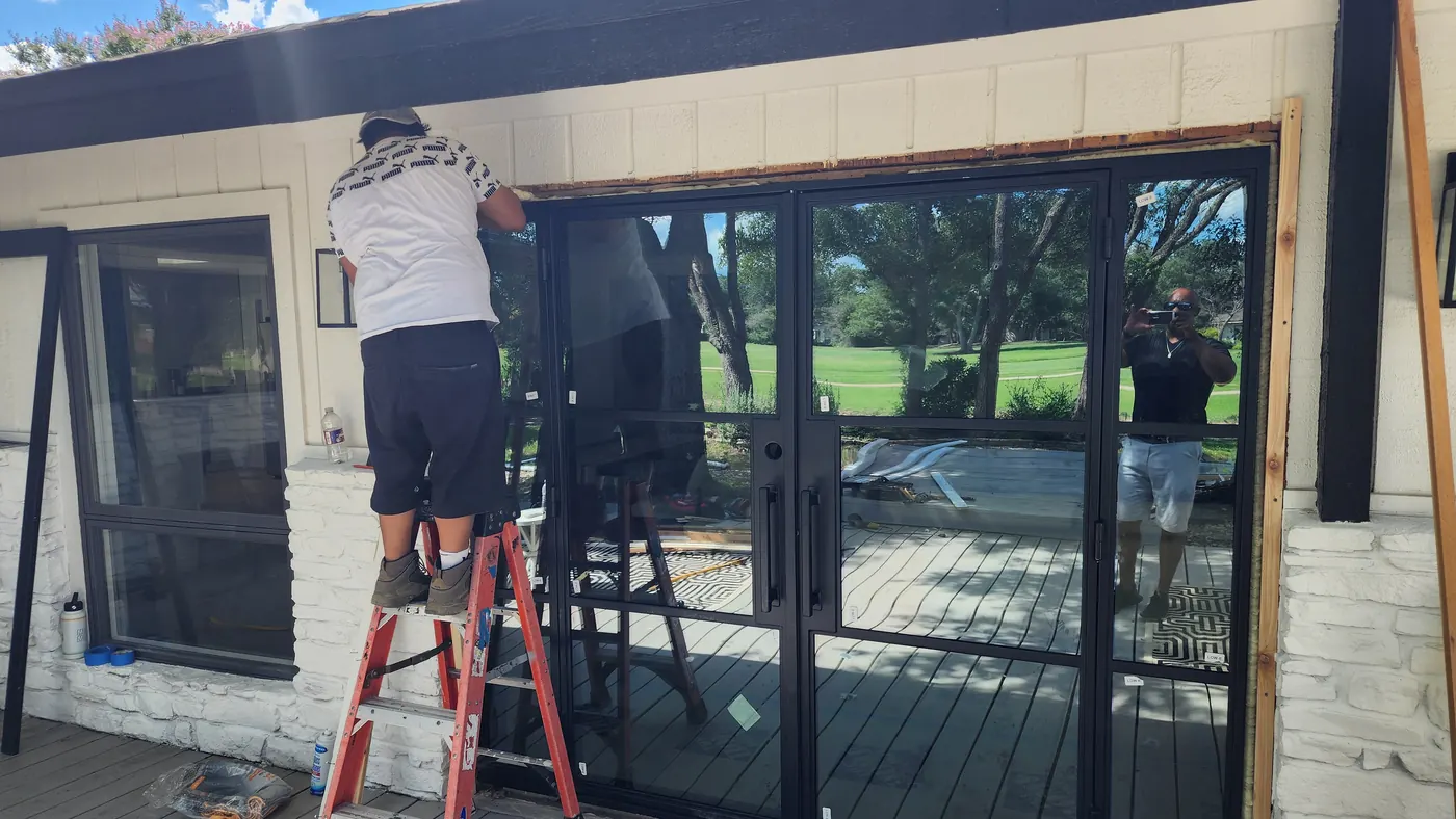 Crew installing a black steel patio door wall across the back of a Lakeway home