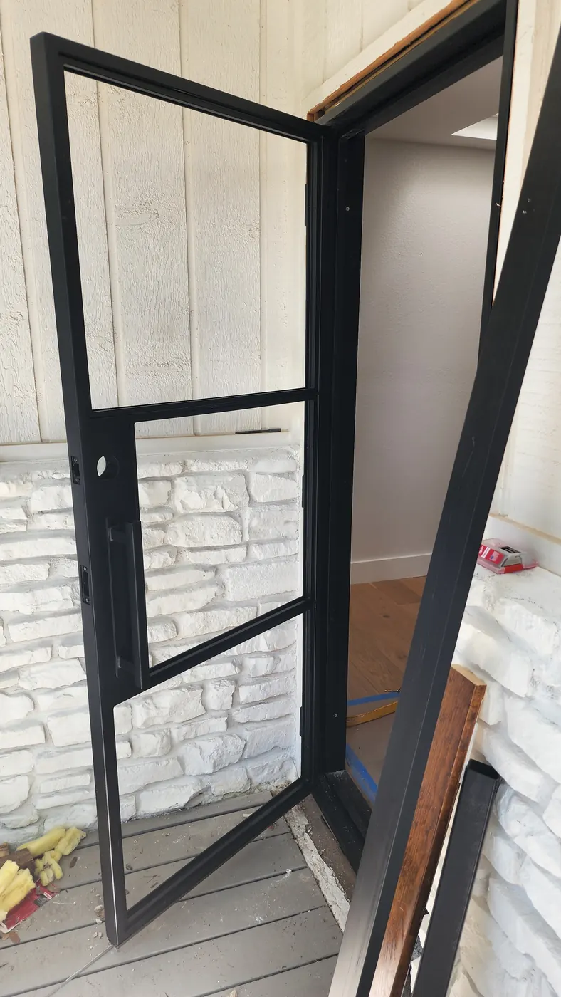 New black steel door leaf being fitted into the opening at a Lakeway home