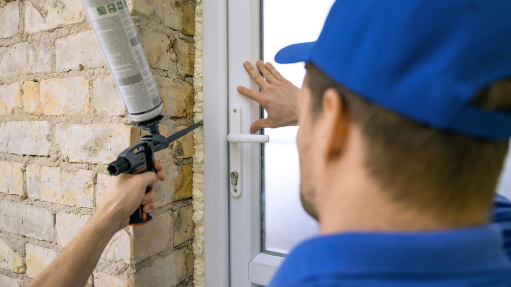 Installer applying low-expansion foam around a door frame in a brick wall